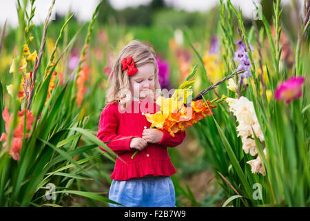 Little Girl holding gladiolus mazzo di fiori. Bambino picking fiori freschi in giardino. Bambini giardinaggio in autunno. Foto Stock