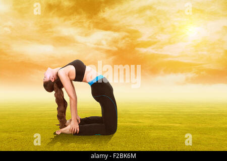 Giovane donna facendo esercizio di yoga su erba con il cielo al tramonto Foto Stock