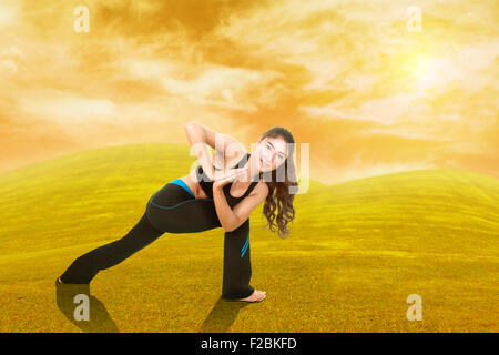 Giovane donna facendo esercizio di yoga su erba con il cielo al tramonto Foto Stock