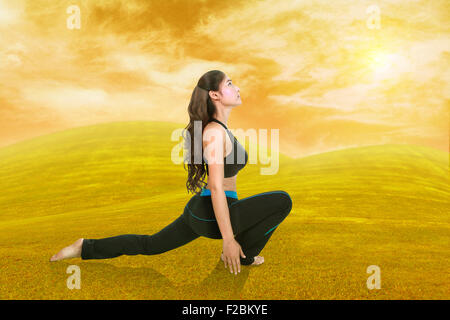 Giovane donna facendo esercizio di yoga su erba con il cielo al tramonto Foto Stock