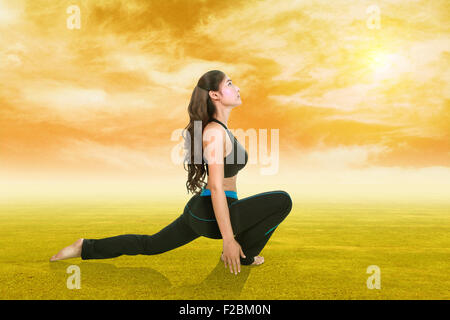 Giovane donna facendo esercizio di yoga su erba con il cielo al tramonto Foto Stock