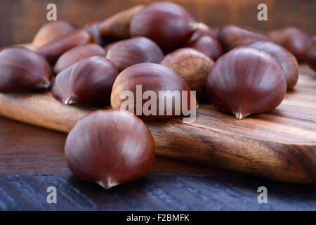 Le castagne sul tagliere di legno contro il legno scuro tavolo rustico. Foto Stock