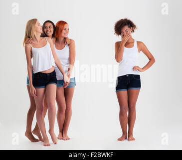 Sconvolto afro american donne in piedi mentre gli amici a ridere con la sua isoalted su sfondo bianco Foto Stock