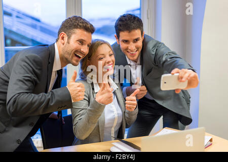 Ritratto di tre persone di affari rendendo pollice mentre prendendo un selfie con lo smartphone Foto Stock