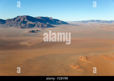Aride pianure del deserto con i cosiddetti circoli di fata e isolato le creste della montagna in corrispondenza del bordo del Namib Desert, vista aerea da un Foto Stock