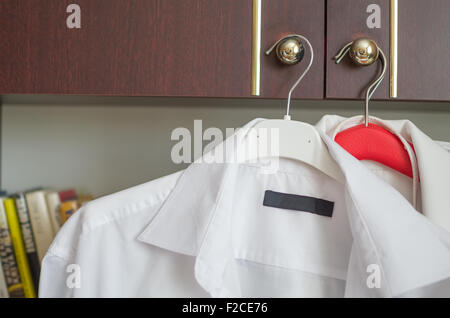Camicie bianche sulle staffe poste sulle maniglie armadio nella parte anteriore dello scaffale Foto Stock