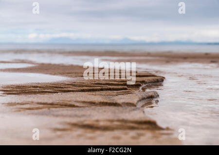 Un basso angolo, la profondità di campo ridotta fotografia di pattern nella sabbia creato dal movimento di acqua nel flusso Foto Stock