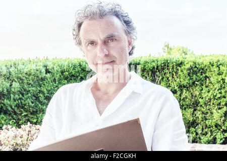 Elegante sportivo senior con la barba di tre giorni e sale e pepe capelli indossa una camicia bianca mentre reding il menù del ristorante Foto Stock