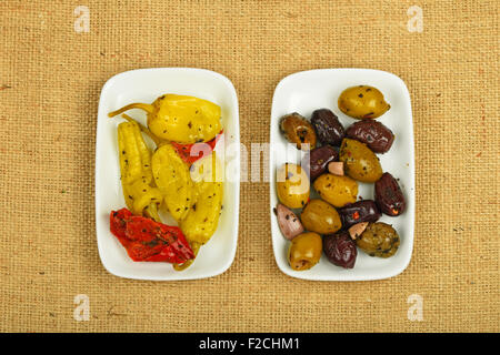 Snack mediterranea del rosso e del verde e delle olive in salamoia pepe verde in due piastre bianche su tela tela di iuta Foto Stock