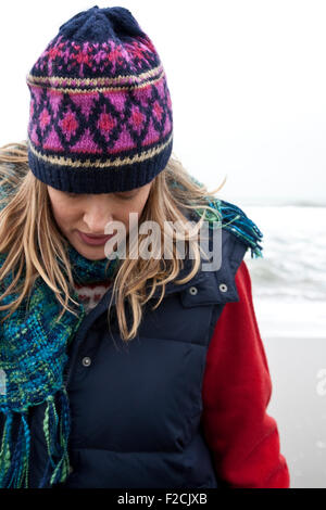 Close-up di giovane donna che guarda verso il basso, indossare abbigliamento invernale in spiaggia Foto Stock