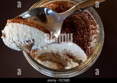 Guardando verso il basso in corrispondenza di un vaso di tiramisù con cucchiaio su sfondo scuro Foto Stock