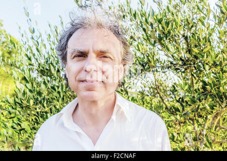 Senior elegante uomo che indossa una camicia bianca tra le foglie degli alberi di olivo Foto Stock