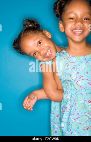Due ragazze sorridenti gemelli identici indossando sundresses blu, uno dietro l'altro in un blu, impostazione di studio Foto Stock
