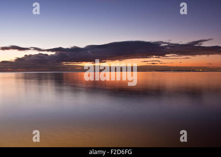 Acqua liscia superficie in arancione tramonto colori con la città di Melbourne luminoso luci a distanza Foto Stock