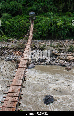 Stretto ponte sospeso oltre il fiume di montagna in Himalaya, Nepal, con una persona che si trova in corrispondenza della estremità lontana del ponte. Foto Stock