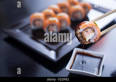 Rotolo di Sushi con crema di formaggio e salmone fritto. E rabboccato con materie di salmone e calce. Essendo prelevato con bacchette da salsa di soia, Foto Stock