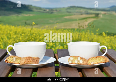 Due tazze di caffè e cantuccini sul tavolo di legno contro il paesaggio toscano, Italia Foto Stock