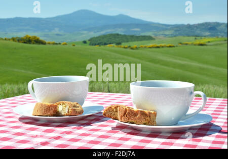 Due tazze di caffè e cantuccini sul panno a scacchi contro il paesaggio toscano, Italia Foto Stock