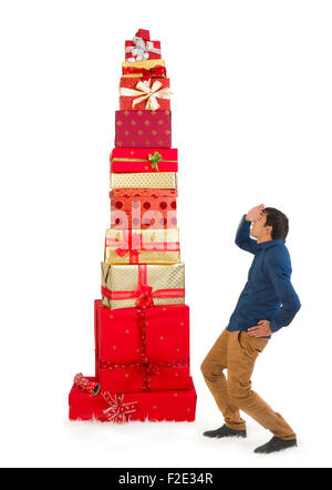 Divertente scena di un giovane uomo che guarda fino a un enorme mucchio di regali di natale Foto Stock