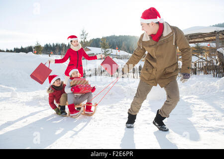 La famiglia felice che porta regali di Natale con slitta Foto Stock