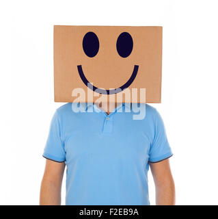 Giovane uomo in piedi con una scatola di cartone sulla sua testa con faccina sorridente su sfondo bianco. Foto Stock