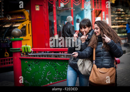 Due giovani femmine tenendo selfie con un bastone in Chinatown, London, Regno Unito Foto Stock