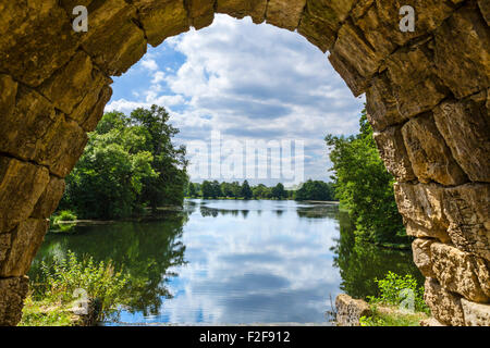 Vista attraverso il passaruota della cascata e rovine artificiali, undici acri di lago, Stowe giardini paesaggistici, Buckinghamshire, Inghilterra, Regno Unito Foto Stock