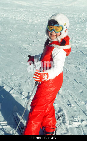 Un simpatico giovane ragazza asiatica in un rosso brillante tuta da sci, blu occhiali da sci e pelliccia bianca cappello sci sorrisi in emozioni come lei è pronto a scendere un coniglietto pendenza su Mt. Alyeska in Alaska, Stati Uniti d'America. Foto Stock