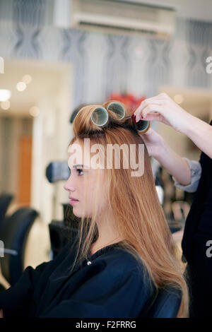 Parrucchiere il rotolamento del cliente in capelli arricciacapelli in salone Foto Stock