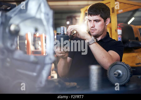 Mechanic esaminando parte nel negozio di riparazioni auto Foto Stock