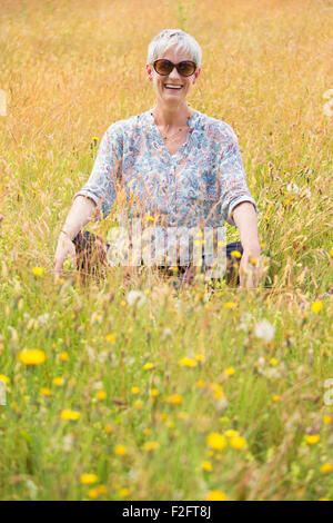 Ritratto senior donna seduta con le gambe incrociate in campo rurale Foto Stock