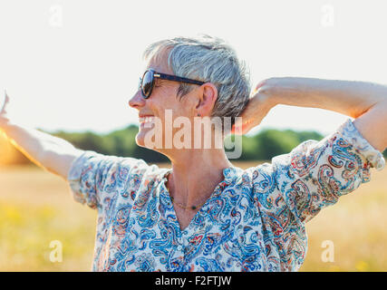 Entusiasta il senior donna con le braccia aperte nel campo soleggiato Foto Stock