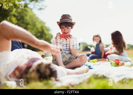 Ragazzo sorridente mangiando anguria sulla coperta in campo soleggiato Foto Stock
