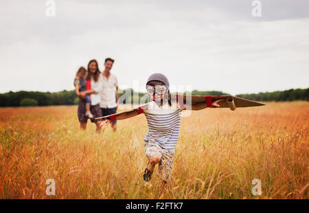 Giocoso ragazzo con ali in aviator cappello e occhiali volanti nel campo Foto Stock