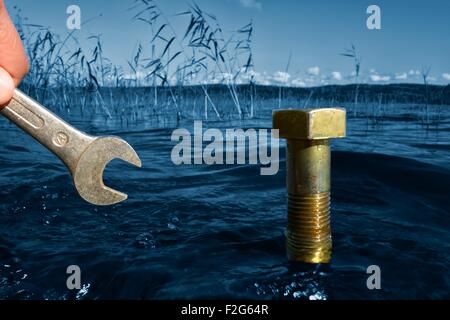 Concetto ambientale: a mano con una chiave di fronte a un bullone di grandi dimensioni in un lago. Foto Stock