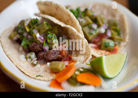 Due carne asada tacos con nopales, chipotle e salsa su una piastra bianca con calce e verdure sottaceto Foto Stock