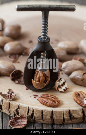 Noci pecan tagliate a rottura in un antico schiaccianoci, circondato da pecan su legno ruvido Foto Stock