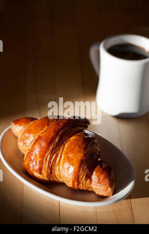 Un lato luminosamente illuminata croissant con una tazza di caffè provenienti al di fuori di un'ombra su un tavolo Foto Stock