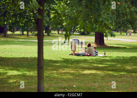 Tre persone irriconoscibili, due ragazzi e una ragazza seduta sul prato di parco sulla giornata di sole. Foto Stock