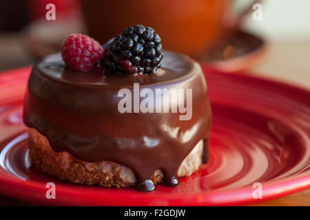 La panna acida cheesecake immersi nel cioccolato e guarnita con un lampone e un Blackberry Foto Stock