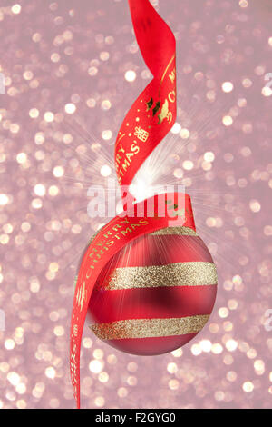 Pallina di natale con nastro rosso su sfondo di confetti. Foto Stock