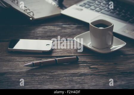 Composizione vintage del moderno tavolo in legno scrivania con computer portatile dello smartphone e la tazza di caffè Foto Stock