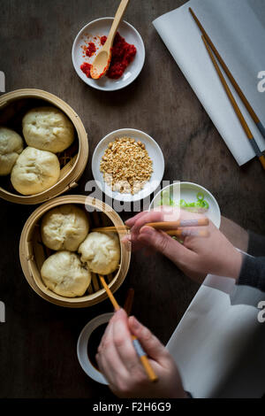 Donna di mani che serve gnocchi di patate al vapore da bambù vaporetti sul tavolo di legno. Vista superiore Foto Stock