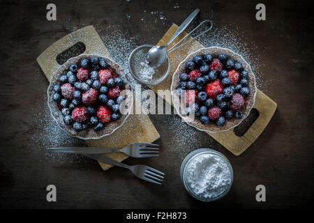 Berry tartetelets con zucchero a velo in piatti di cottura su piastre di legno con il buratto e torta forche. Vista superiore Foto Stock