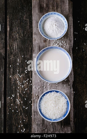 Stile cinese ciotole con latte di riso, farina di riso e riso imbevuto su un vecchio sfondo di legno con grani di riso di cui sopra. Vista dall'alto. Foto Stock