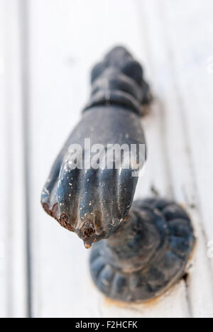 Vecchio arrugginito nero a mano a forma di porta respingente sul bianco porta in legno closeup. Lefkara. Cipro. Foto Stock