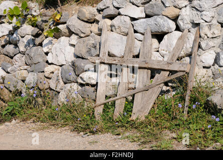 Una ruvida gate rustico si appoggia contro una pietra a secco parete. Theth, Thethi, Albania. Foto Stock