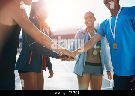 Inquadratura di un gruppo di giovani sportivi con medaglie accumulando le loro mani mentre in piedi in un huddle. Team di Successo di atleti con t Foto Stock