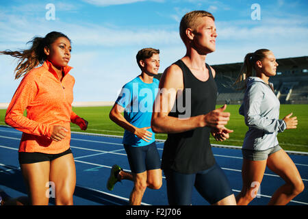 Gruppo di multirazziale atleti professionisti la pratica della corsa in stadium. Maschio e femmina atleti correndo insieme sulla pista