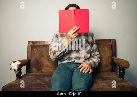 Giovane uomo sul divano con libro Foto Stock